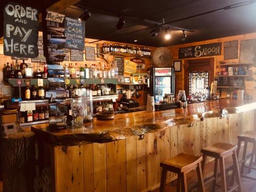 A rustic bar with wooden counters, shelves of liquor, and a cozy saloon atmosphere. Signs for ordering and payment are visible.