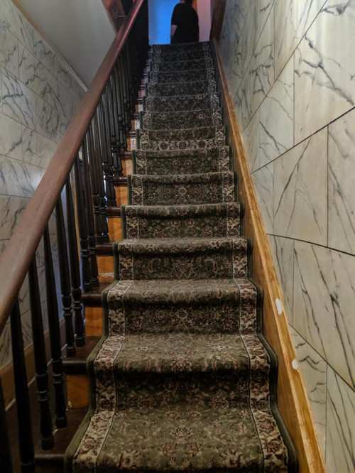 A carpeted staircase with a wooden railing, leading up to a dimly lit area at the top.