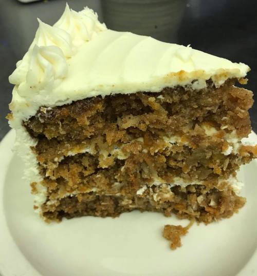 A slice of layered cake with cream frosting, showcasing moist, crumbly layers and decorative swirls on top.
