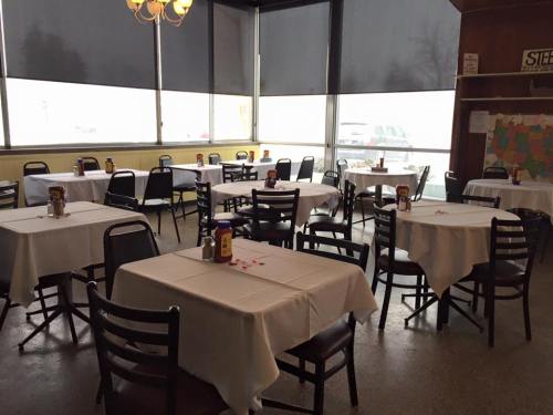 Empty restaurant with white tablecloths, chairs, and condiments on tables, large windows showing a snowy view outside.