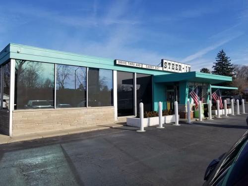 A retro-style diner with a turquoise exterior, featuring a drive-thru and American flags outside.