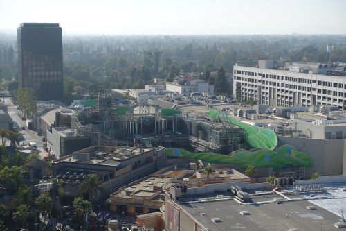Aerial view of a construction site surrounded by buildings and greenery, with a hazy skyline in the background.