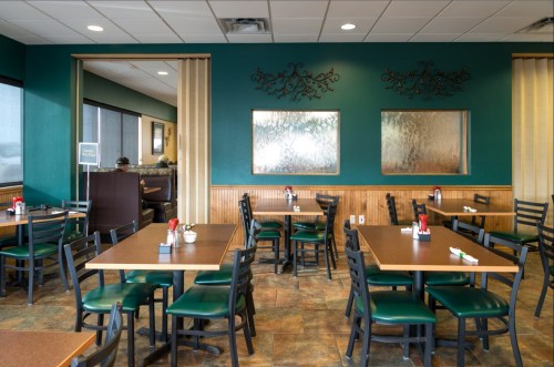 Interior of a casual dining restaurant with empty tables, green walls, and decorative mirrors.