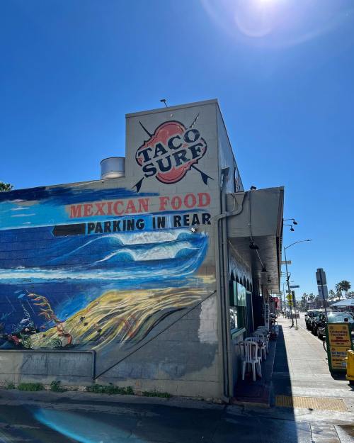 A colorful mural on a building advertising "Taco Surf" and "Mexican Food," with a clear blue sky above.
