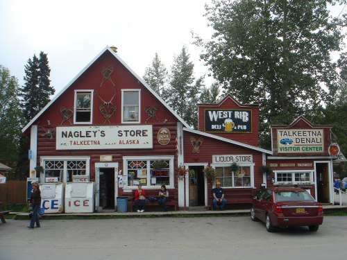 A red wooden building with signs for Nagley's Store, a liquor store, and the Talkeetna Denali Visitor Center in Alaska.