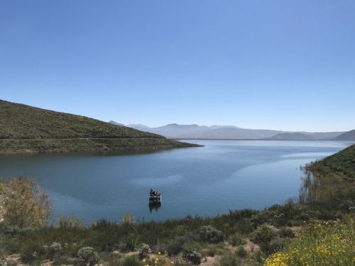 A serene lake surrounded by green hills under a clear blue sky, with a small boat in the water.