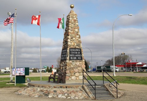 A stone monument marking the Geographical Center of North America in Rugby, ND, with flags of the USA, Canada, and Mexico.