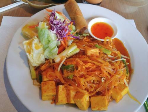 A plate of Pad Thai with tofu, spring rolls, fresh vegetables, and a small bowl of dipping sauce.