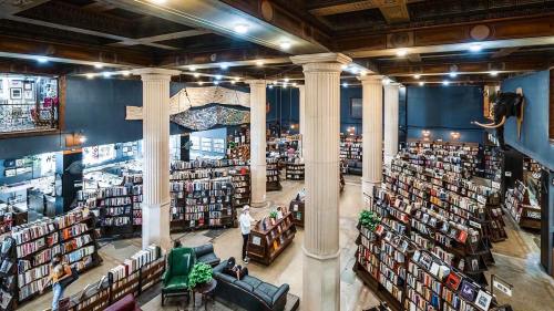 A spacious bookstore with tall columns, filled with bookshelves and cozy seating areas, bustling with visitors.