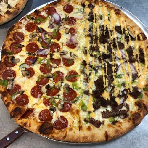 A large pizza divided into two halves: one with pepperoni, vegetables, and cheese, the other with beef and drizzled sauce.