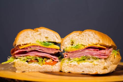 A freshly cut sandwich filled with layers of ham, cheese, lettuce, and tomato on a wooden board.