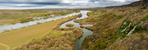 Aerial view of a winding river surrounded by lush greenery and rolling hills under a cloudy sky.