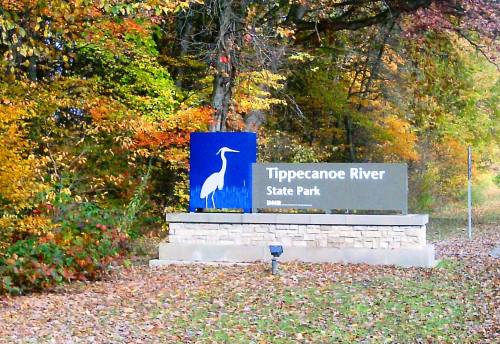 Sign for Tippecanoe River State Park, featuring a heron silhouette and surrounded by colorful autumn foliage.