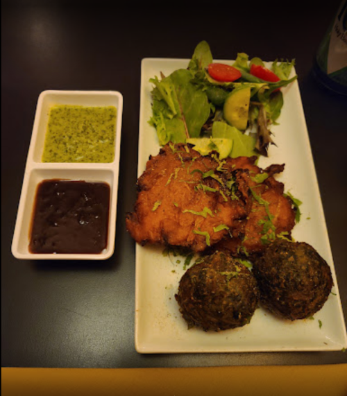 A plate with fried items, two green balls, a fresh salad, and two dipping sauces in small containers.