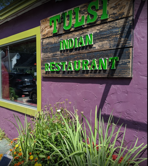Sign for "Tulsi Indian Restaurant" on a purple wall, surrounded by colorful flowers and greenery.