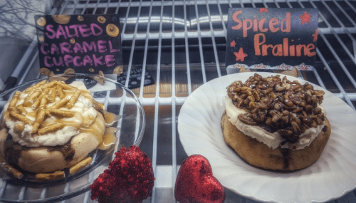 Two delicious cupcakes: one salted caramel with drizzled caramel, the other spiced praline topped with pecans, displayed on a shelf.