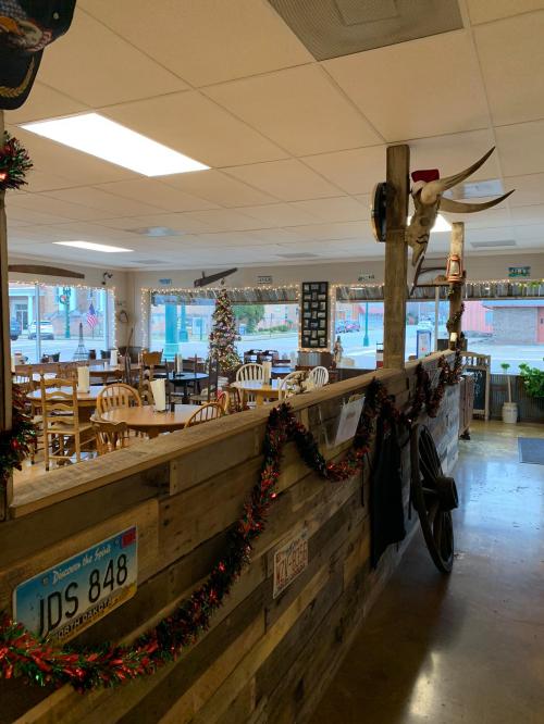 Interior of a rustic restaurant decorated for the holidays, featuring wooden walls, a Christmas tree, and festive garlands.