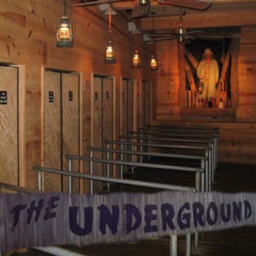 Interior of a rustic attraction with wooden walls, lanterns, and a sign reading "The Underground" near waiting lines.
