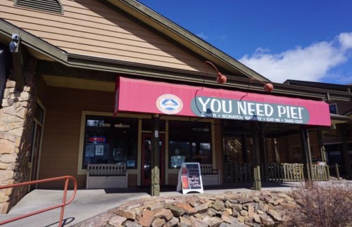 Exterior of a restaurant with a red awning that reads "YOU NEED PIE!" and a sign indicating it's open for take-out.