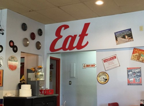 Interior of a diner featuring a large "Eat" sign, vintage decor, and various wall signs.