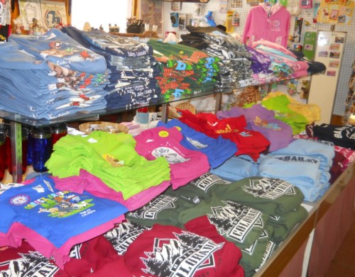 A display of colorful t-shirts stacked on tables in a shop, featuring various designs and sizes.