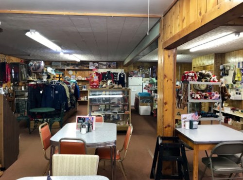 A cozy shop interior with wooden walls, displaying clothing, gifts, and a dining area with tables and chairs.