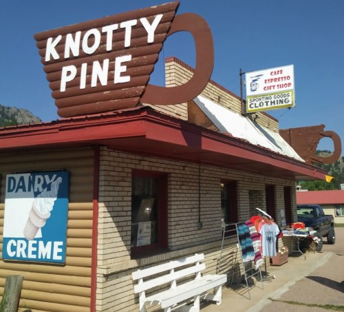 A rustic building with a sign reading "Knotty Pine," featuring a café and sporting goods shop, with merchandise outside.