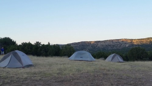 Three tents set up on a grassy field with a mountainous landscape in the background under a clear blue sky.