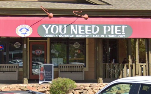 A diner with a red awning that reads "YOU NEED PIE!" and a sign for take-out and coffee.