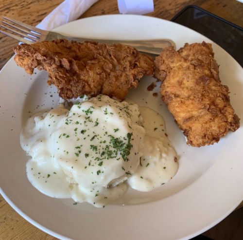 Plate of fried chicken with two pieces and a serving of mashed potatoes topped with creamy gravy and parsley.