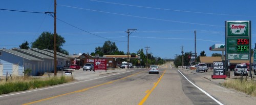 A rural highway scene with a Sinclair gas station, shops, and a market, under a clear blue sky.
