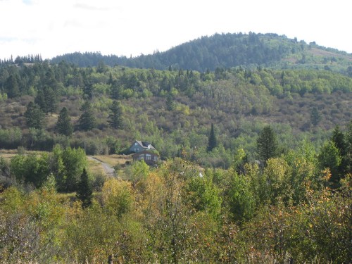 A scenic view of a house nestled among lush green hills and trees under a partly cloudy sky.