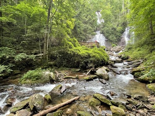 A serene forest scene featuring a waterfall cascading down rocks, surrounded by lush greenery and a flowing stream.