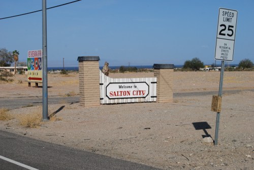 Welcome sign for Salton City, with a speed limit sign nearby, set in a dry, desert landscape.