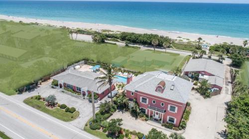 Aerial view of a beachside property with a pool, tennis court, and palm trees, overlooking the ocean.