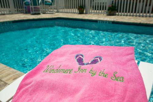 A pink towel with "Windmen Inn by the Sea" embroidered, resting by a sparkling blue pool.