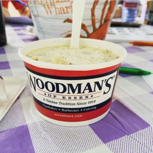 A cup of clam chowder from Woodman's of Essex, placed on a checkered tablecloth.