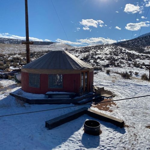 A yurt surrounded by snow, with mountains and a blue sky in the background.