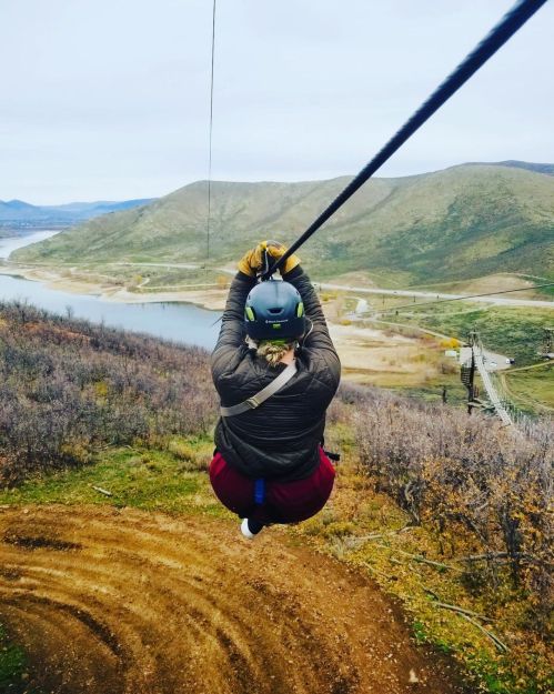 A person zip-lining over a scenic landscape with hills and a body of water in the background.