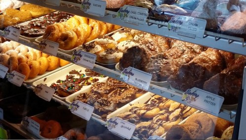 A display case filled with various donuts and pastries, including chocolate-covered, cream-filled, and apple fritters.
