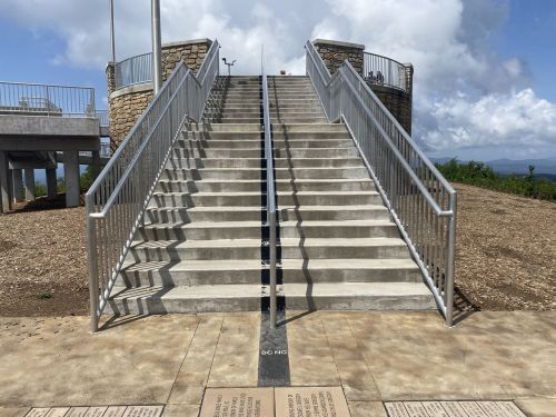 Concrete stairs with railings lead up to a viewpoint, surrounded by a grassy area and cloudy sky.