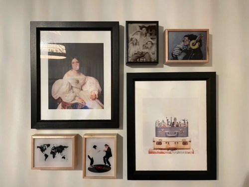 A collage of framed artworks on a wall, featuring portraits and illustrations in various styles and sizes.