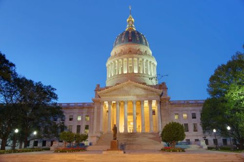 The West Virginia State Capitol building illuminated at dusk, featuring a large dome and grand entrance steps.