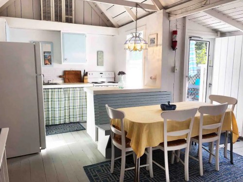 Bright, airy kitchen with a dining table, white chairs, and modern appliances, featuring light wood and pastel decor.