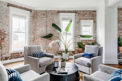 A cozy living space with two gray chairs, a round black table, and a large plant, set against exposed brick walls.