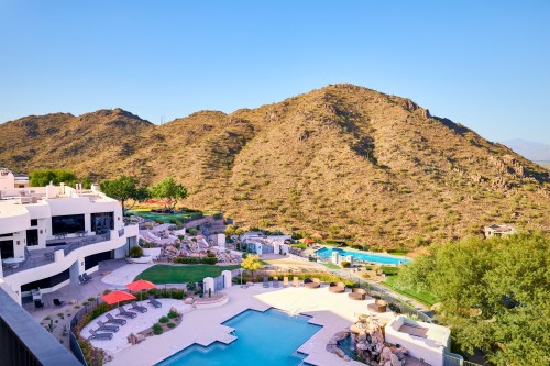 A scenic view of a resort pool area surrounded by mountains and greenery under a clear blue sky.