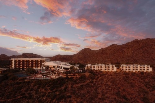 A scenic view of a resort nestled in mountains at sunset, with vibrant clouds and warm colors in the sky.