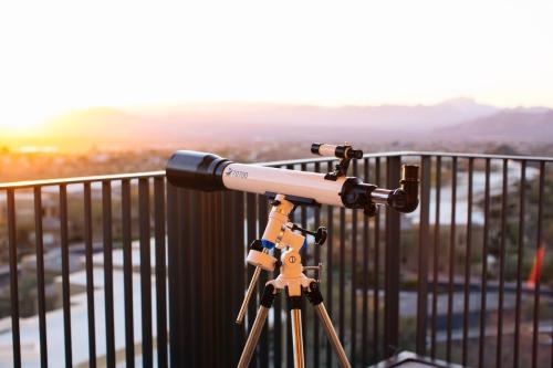 A telescope on a balcony overlooking a sunset landscape with mountains in the distance.