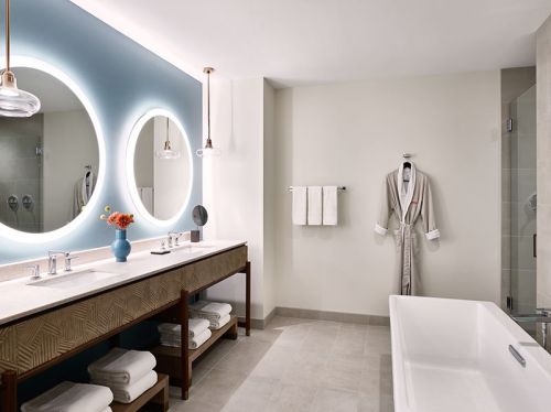 Modern bathroom featuring a double sink, large mirrors, a freestanding tub, and neatly arranged towels.