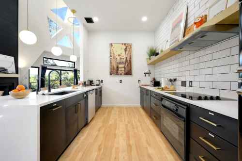 Modern kitchen with white and black cabinetry, a large window, and wooden flooring, featuring stylish decor and appliances.